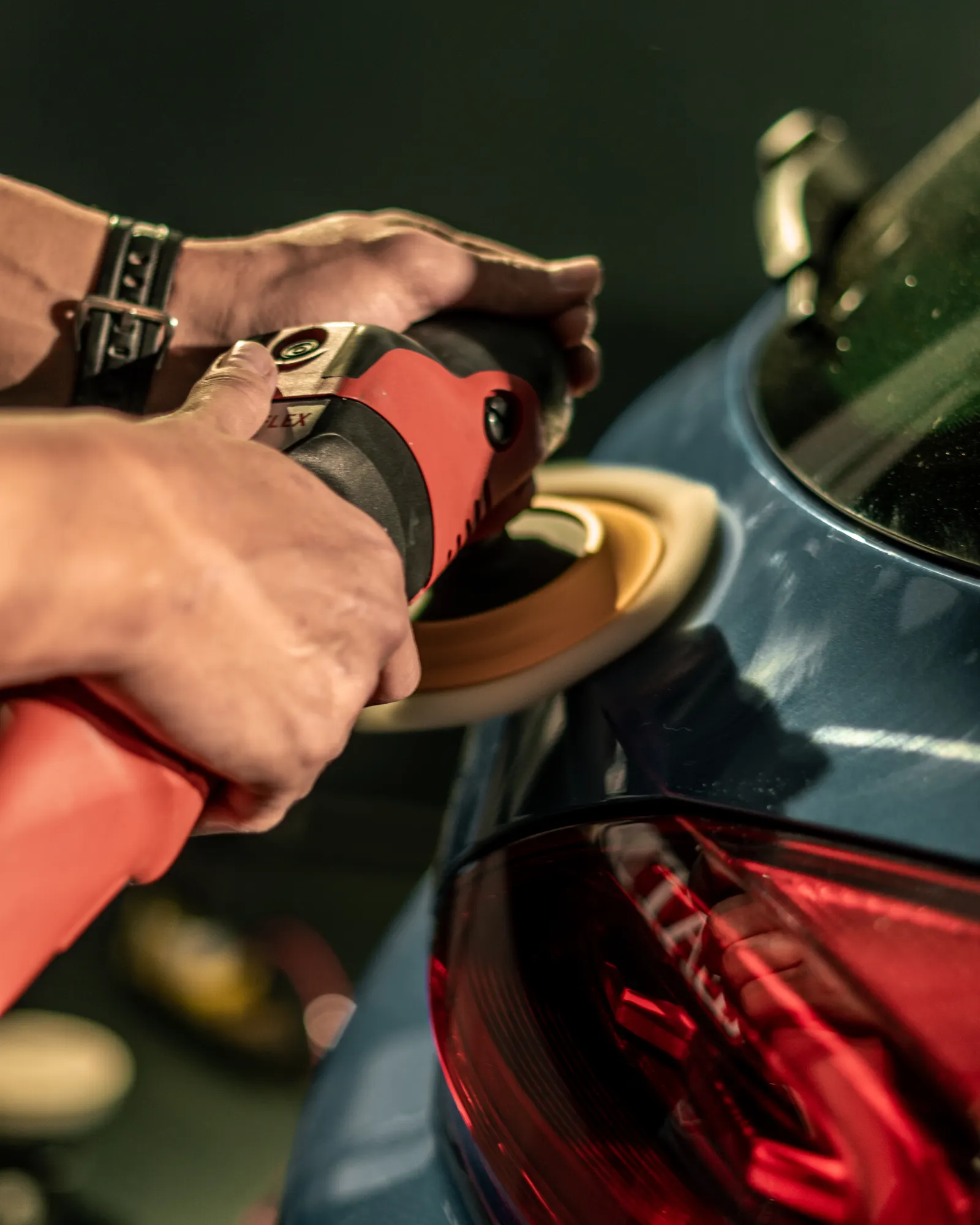 Hands guiding a machine polisher over automotive paint