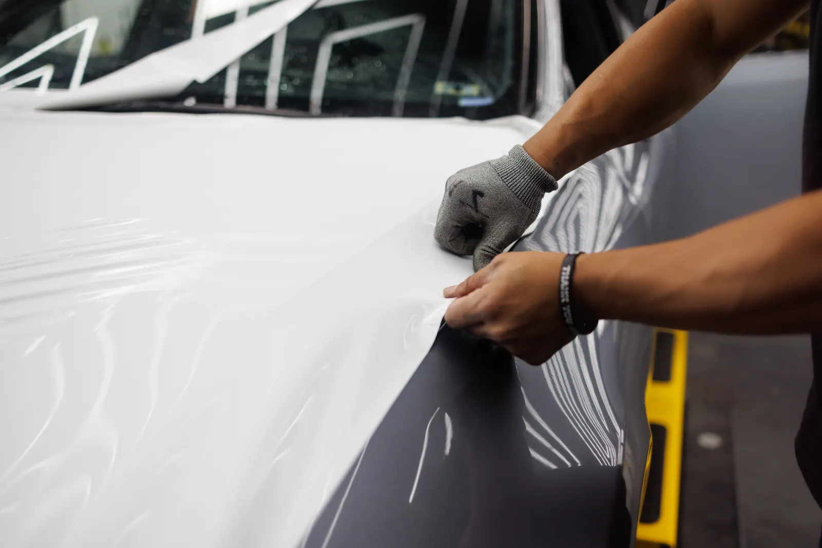 Gloved hands fitting vinyl film to a vehicle hood